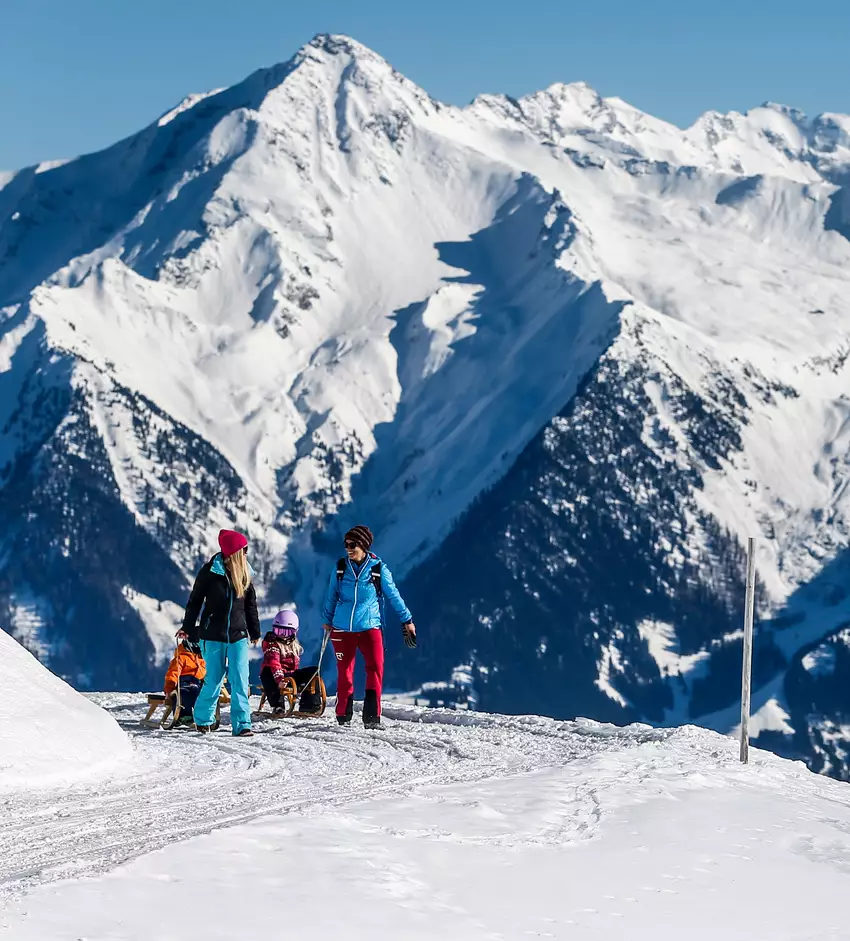 Familie beim Rodeln mit Bergkulisse